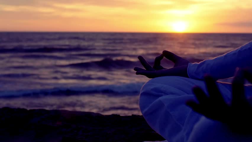 Healthy young woman in front of the sea in lotus pose, meditating at beach on sunset. Concept of healthy life, relaxing, meditating and yoga exercise.