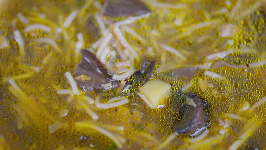 Soup with noodles. Steaming bowl of mushroom noodle soup with toppings and oil droplets. Detailed view of simmering mushroom noodle soup garnished with herbs and oil