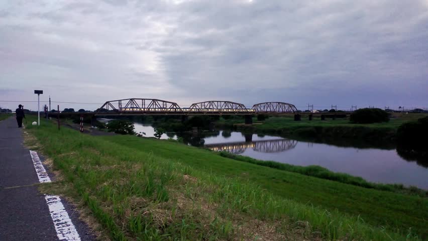 Emotional twilight river landscape with a train crossing an iron bridge and a person walking a dog on the embankment