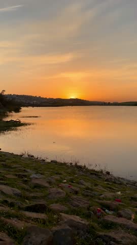 Beautiful golden sunset over a calm lake with water reflections and cloudy sky, real time footage.
