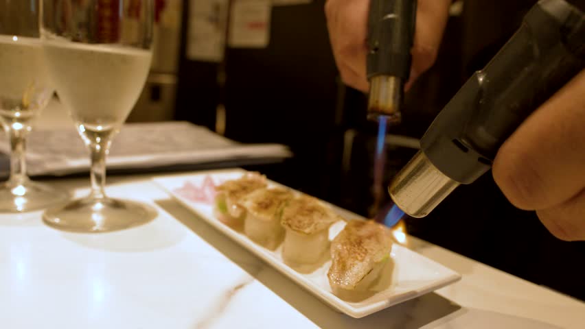 A chef uses a blue flame blowtorch to sear fresh nigiri sushi at a restaurant