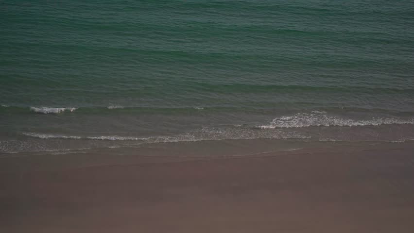 High angle timelapse of gentle turquoise ocean waves washing onto an empty sandy tropical beach on a cloudy day.