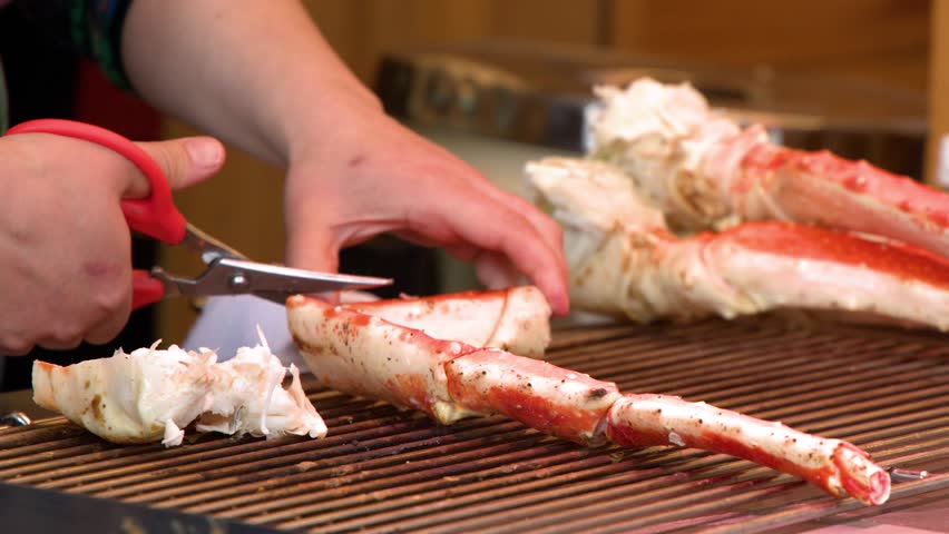 Close-up of hands using scissors to cut grilled king crab legs at a street market.