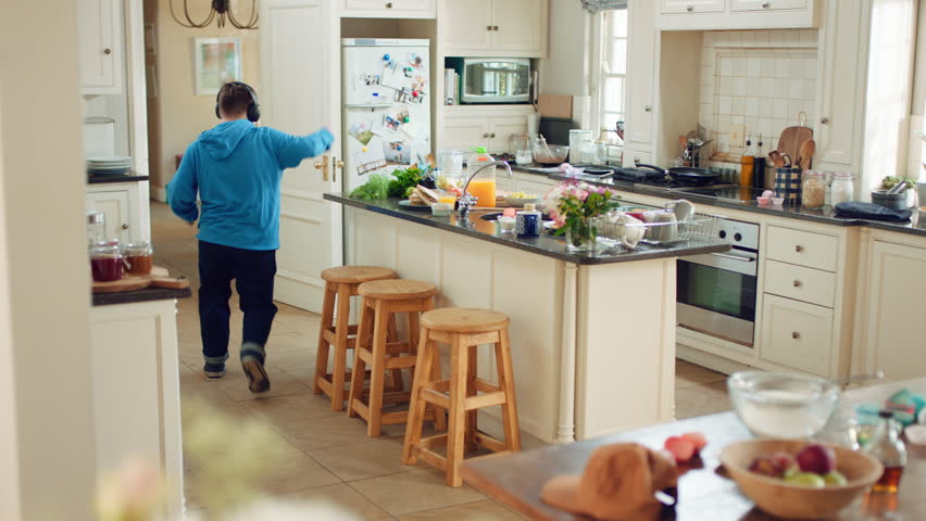 Dancing, headphones and man in kitchen with energy for performance, audio or playlist in home. Tech, movement and person with down syndrome for hobby, entertainment and weekend fun in apartment