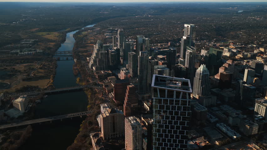 Aerial reverse and slow pan over downtown Austin, Texas, with the full sweep of Lady Bird Lake revealed beneath the Waterline tower. The Long Center, Auditorium Shores, and the Congress Avenue, First Street, and Pfluger bridges anchor the foreground while dormant winter foliage and dry grass cover the south shore. The Hill Country horizon stretches across the back. Seamless playthrough when purchased with Parts 1, 2, and 3. Part 4 of 4.