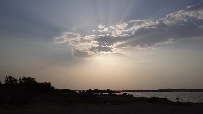 Sunlight streaming through clouds over a tranquil lake landscape during late afternoon.