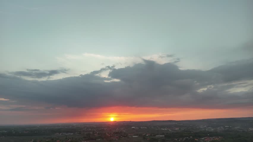 Aerial View of Dramatic Sunset Sky with Bright Orange Sun Over Silhouetted Village Landscape