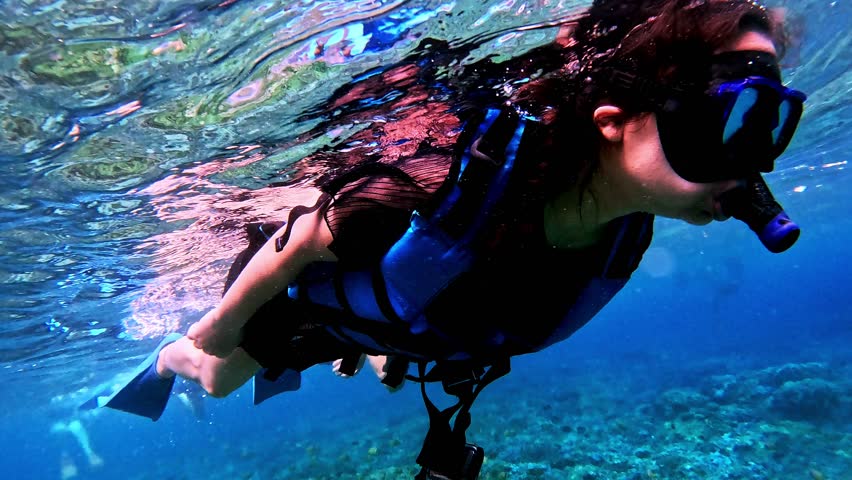 People snorkeling in clear tropical ocean water near Nusa Penida, Bali, enjoying marine life and underwater adventure.