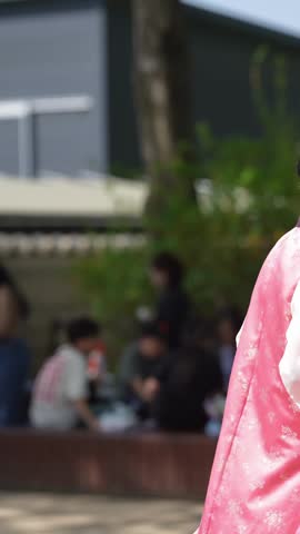 Pink kimono draped over shoulders. Back view, elegant fabric. Dark blue kimono with gold trim. Hair adorned with delicate hairpins. Couple walks away, peaceful. Outdoor garden, soft daylight