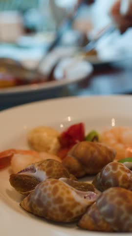 Static close-up shot of sea snails and shrimp on a white plate at a buffet