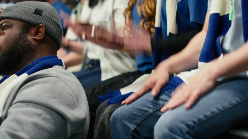 Diverse blue team soccer fans clapping and cheering from stands while crowd leader unites them with megaphone during live football match, energetic atmosphere, cheering for national team.