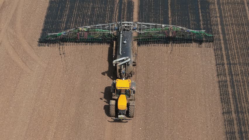 Tractor applying liquid organic manure fertilizer in agricultural field. Precision farming machinery improving soil fertility, crop yield, farm productivity. Sustainable agriculture, agribusiness