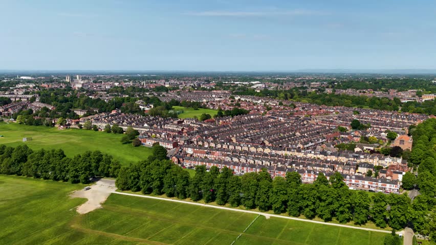 Aerial drone footage of York North Yorkshire England showing rows of terraced housing green parkland and the distant York Minster skyline beneath a clear blue sky in summer daylight