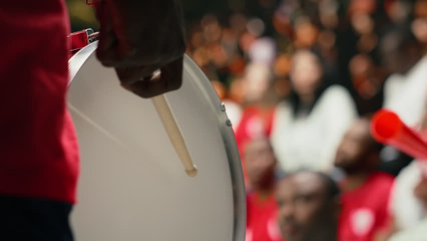 Supporter group leader playing fan drums and leading chants, creating intense energy from fan section during football match, diverse sports fans with face paint and raised scarves.