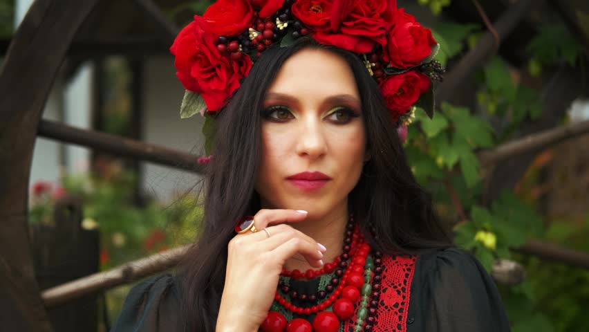 portrait gorgeous fashion model authentic woman beauty face thoughtful makes a decision. brunette long dark hair. Wreath red crown roses flowers ethnic black dress beads. evening makeup sexy eyes lips
