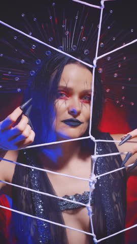 Portrait fantasy gothic woman art creative halloween make-up dark lips cobweb painted on face. Girl queen spider shows hand gesture of invitation, beckons into trap. Black dress costume. Night room.