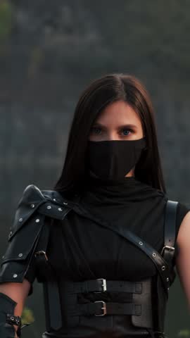 Portrait fantasy woman warrior assassin holds dancing with two burning blade daggers in hands, flame fire. Dancer hiding face behind mask. Armed sexy girl. Black costume. Halloween concept 4k footage