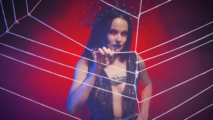 Portrait fantasy gothic woman art creative halloween make-up dark lips cobweb painted on face. Girl queen spider shows hand gesture of invitation, beckons into trap. Black dress costume. Night room.