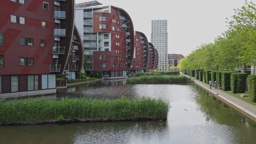 Den Bosch, Netherlands – 9 May 2026: Modern waterfront residential district with contemporary apartment architecture.
Modern residential apartment buildings surround a calm waterfront in Den Bosch, the Netherlands, during a sunny spring day. The curved architecture, green urban landscaping and reflective water create a contemporary European cityscape focused on sustainable urban living and modern city development.