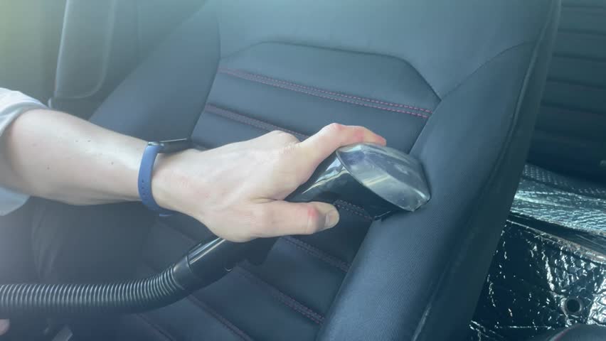 Close up of a person cleaning a black fabric car seat cover with red stitching using a professional extraction vacuum cleaner nozzle, detailing auto interior care. High quality 4k footage