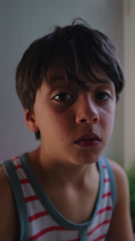 Young child facing camera with subdued gaze highlighting introspection, loneliness and calm reflective mood in soft indoor light