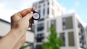Hand holding house keys with My First Home keychain near modern apartment building. Property ownership and first real estate purchase concept. - Powered by Shutterstock - Get 15% off with code: PIKWIZARD15