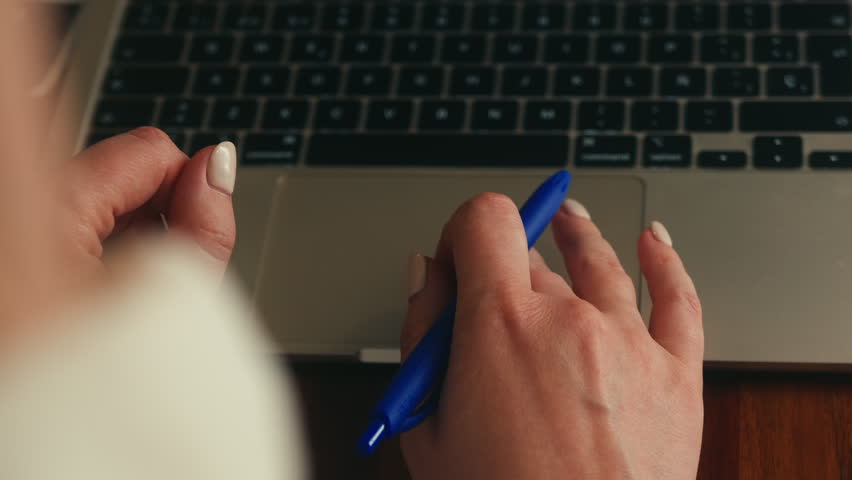 Close-up of female hand holding a pen while working on a laptop. Business planning, online work, studying and productivity concept. High quality 4k footage