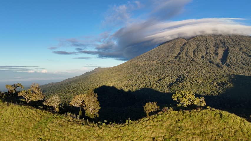 Lush Mountain Landscape with Rolling Green Hills and Cloud-Capped Peak under a Clear Blue Sky at Dawn