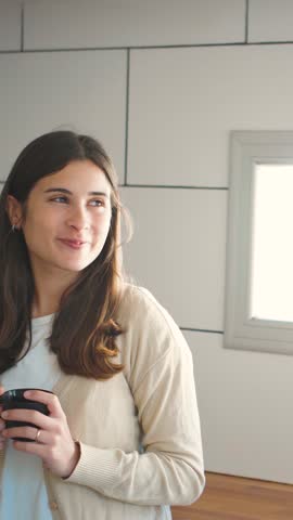 4K video of a young Hispanic couple drinking coffee while laughing and watching social media reels on their mobile phone. Concept of everyday lifestyle, emotional wellbeing, and a healthy romantic relationship.
