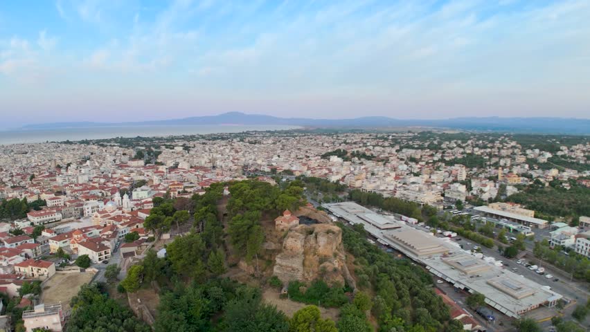 Aerial drone footage of Kalamata Castle hill overlooking the city of Kalamata in the Peloponnese, Greece. The scene captures historic stone ruins, a small hilltop church, pine trees, old walls, nearby red tiled rooftops, dense urban neighborhoods, the Messinian Gulf, distant mountain ranges and a soft pastel sky near sunset.

This clip is suitable for travel videos, tourism projects, documentaries, historical content, architecture edits, cultural heritage stories, Mediterranean destination films, Greek city visuals and scenic establishing shots of southern Greece. The view combines the old fortress hill with the modern city, coastal horizon and surrounding landscape, giving a strong sense of place and atmosphere.