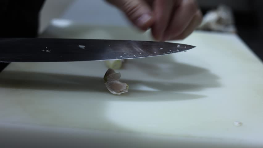 Chef crushing and peeling garlic cloves with a knife