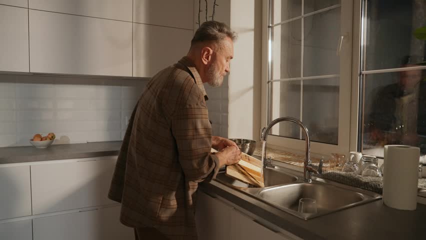 A man is holding a sponge and cleaning a cutting board