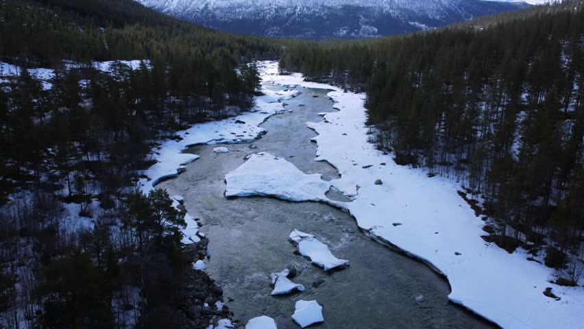 Forward push along a river through a mountainous winter landscape with snow-covered banks and ice floes in Norway.