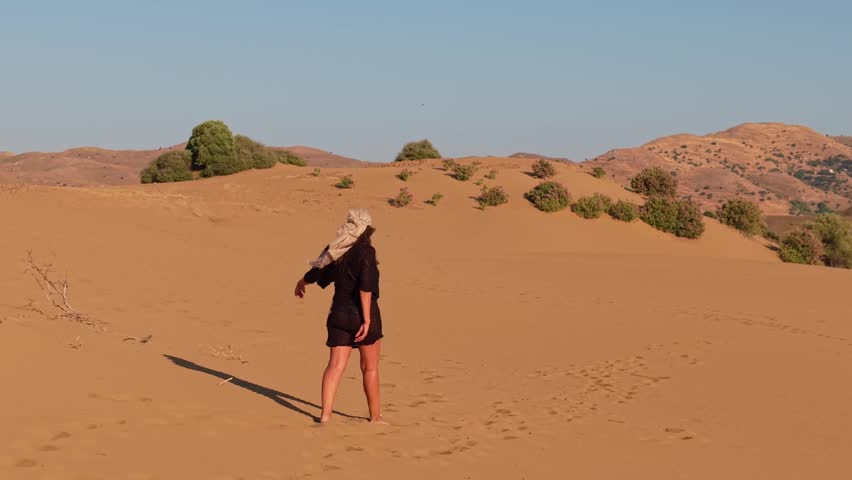 A woman in black walking through the Ammothines desert in Lemnos, capturing golden sand dunes and a minimal landscape under a clear sky.