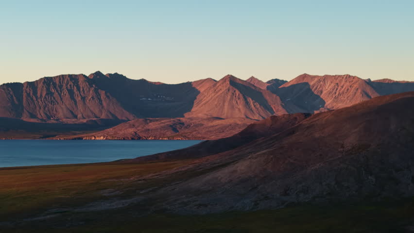 Aerial drone footage shows tracking past peaks above Gilmimyul Bay and Provideniya. Evening sun lights Chukotka Russia ridge while calm lake lies below. Epic remote destination for adventure travel