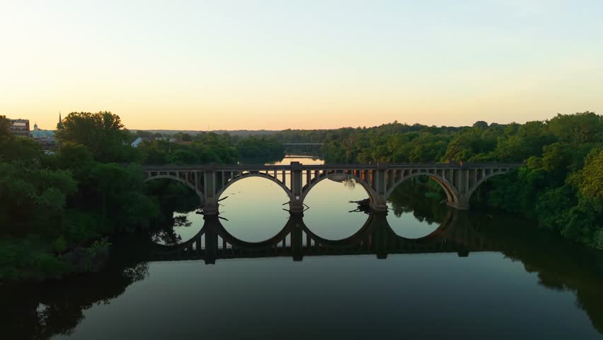 Fredericksburg, Virginia, stunning 4K aerial drone video over the glassy Rappahannock River toward the historic Railroad Bridge, at golden hour sunset.