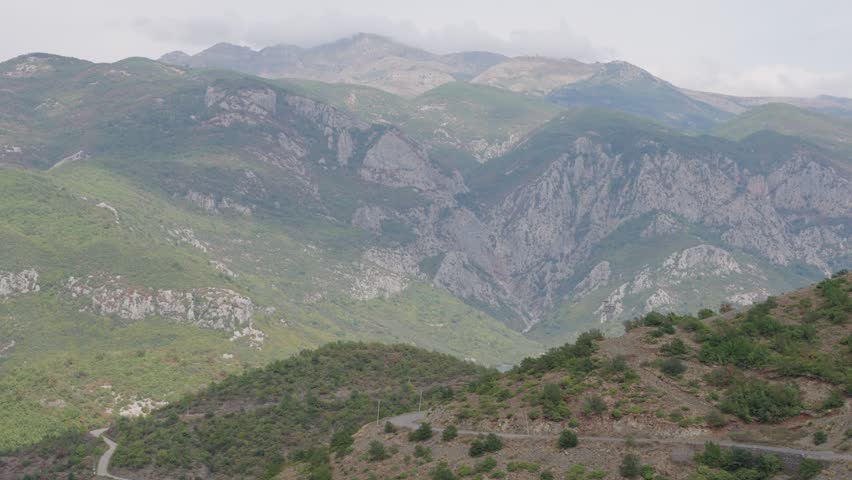 Mountain landscape above winding road beneath cloudy sky in Montenegro, handheld static