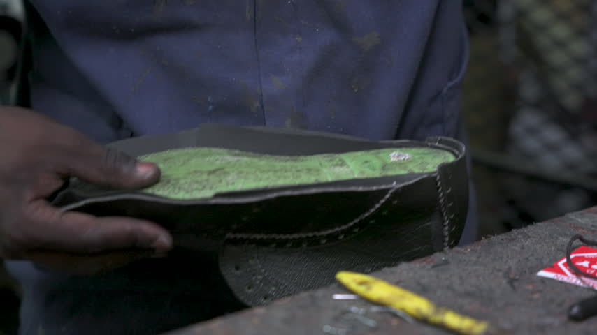 A craftsman uses tools to shape and assemble a leather shoe. The focus is on the intricate details and skill. Ideal for content on traditional craftsmanship or artisanal skills.