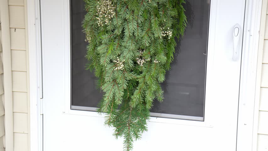 medium wide shot Festive Christmas wreath with ribbon bow hanging on front door, filmed from bottom up. Holiday home decoration, cozy winter atmosphere, Christmas and New Year celebration.
