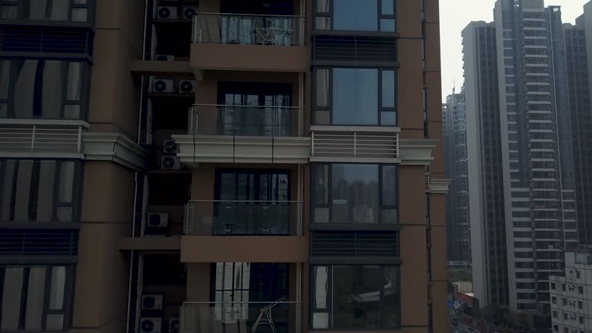 High altitude shot revealing long urban road with moving cars between dense residential blocks. Modern architecture in Chinese metropolis featuring tall glass towers under foggy morning sky.