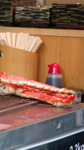 Close-up shot of a street food vendor cutting grilled king crab legs using red scissors.