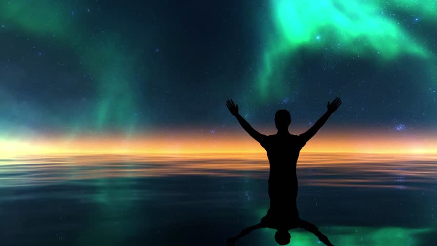 the silhouette of a man standing in the water with both hands raised upwards, overlooking a very stunning natural view. In the background, the night sky is decorated with the green aurora borealis (northern lights) phenomenon which dances beautifully among the expanse of sparkling stars.