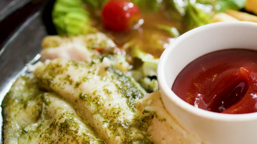 A hand dips a golden french fry into a bowl of red tomato ketchup sauce