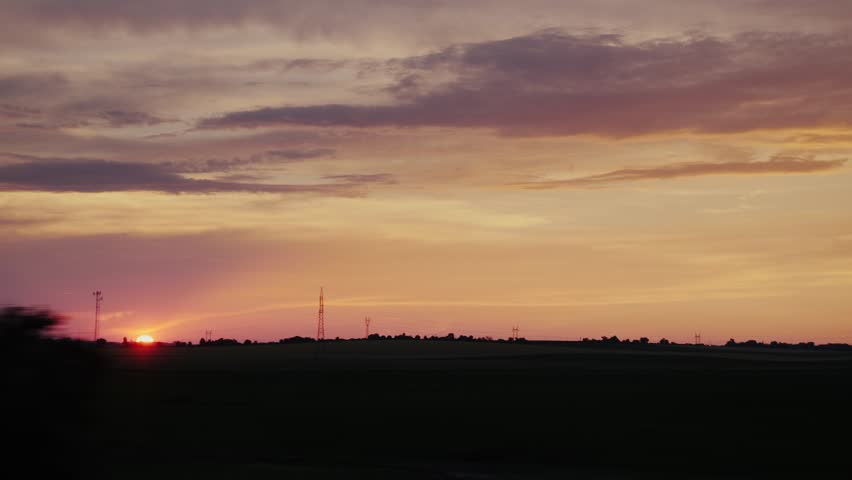 Dramatic sunset with electrical towers on rural field landscape.
