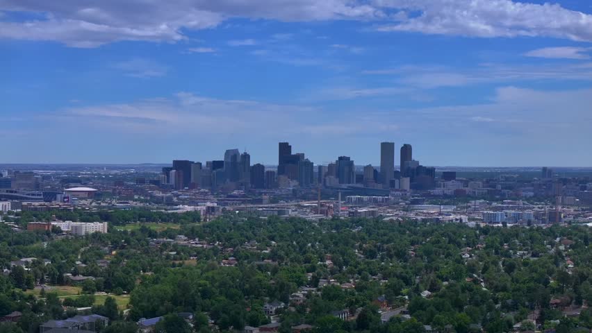 High angle wide shot of Denver Colorado skyline featuring modern architecture buildings and urban greenery. Aerial footage captures metropolitan landscape with residential trees and city life.