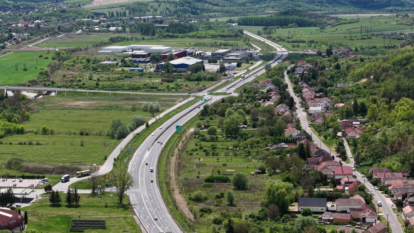 An elevated aerial view capturing a highway passing through a suburban landscape with residential houses and surrounding green farmland areas.