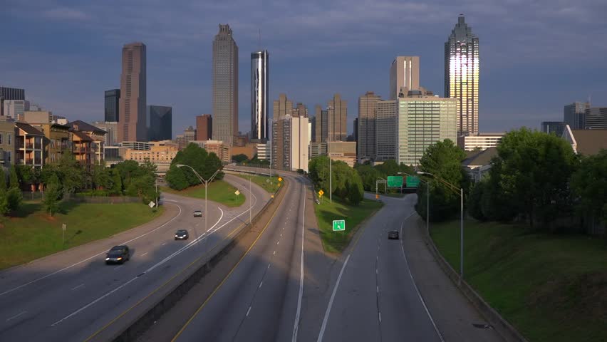 Dynamic wide shot showcasing urban cityscape of Atlanta Georgia at sunrise featuring historic skyscrapers and busy metropolitan freeway with cars traveling towards downtown district during dawn.