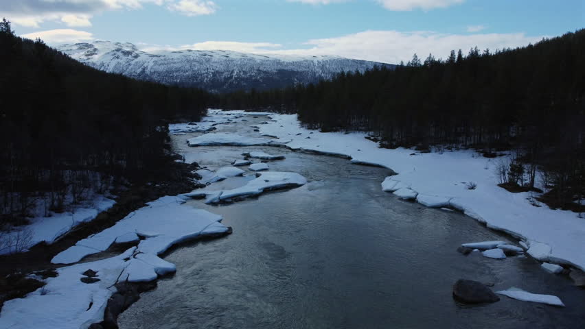 Forward push along a river with snow-covered banks, ice floes, and distant snow-capped mountains in Norway.
