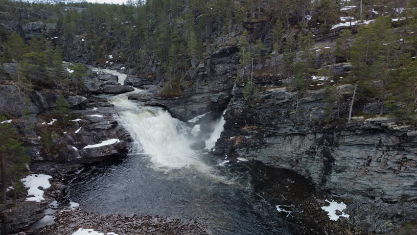 Waterfall cascading into a river pool surrounded by rocky cliffs and coniferous trees in Norway.