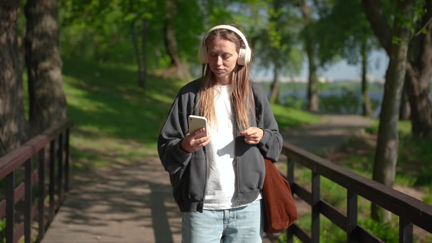 Woman walking on bridge in park during video call and smiling
